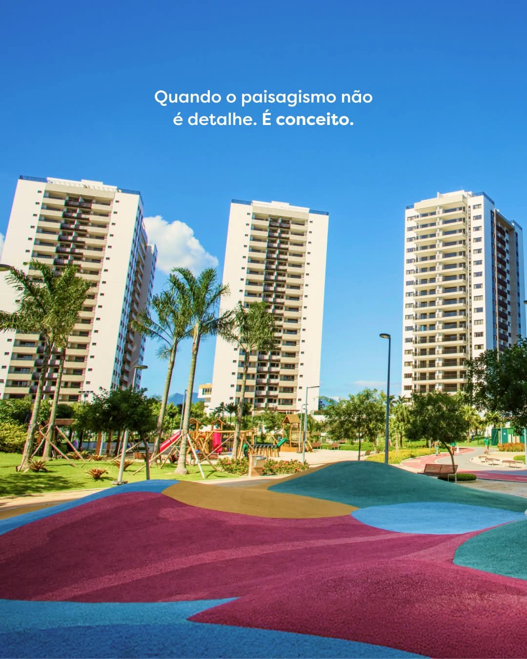 três torres residenciais altas com playground colorido, palmeiras e área verde num dia ensolarado de céu azul 
